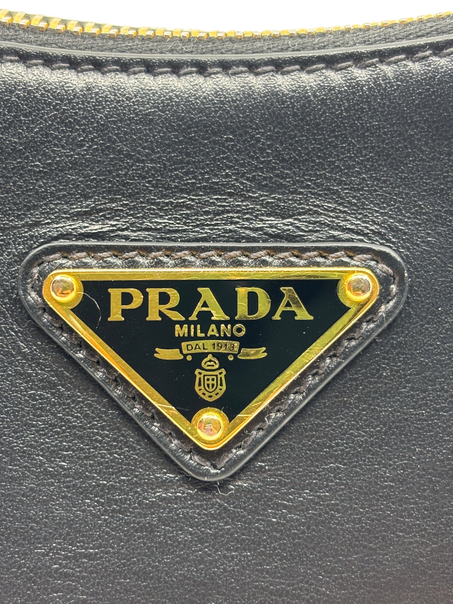 Posh Purse Co. Prada Arqué bag featuring the iconic gold-tone triangular logo plaque on smooth black leather.