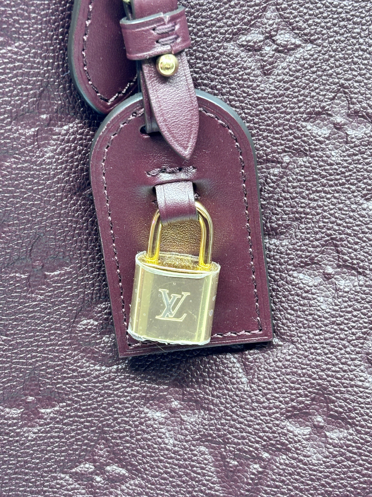 Posh Purse Co. Louis Vuitton maroon leather luggage tag with gold padlock and embossed monogram detail.