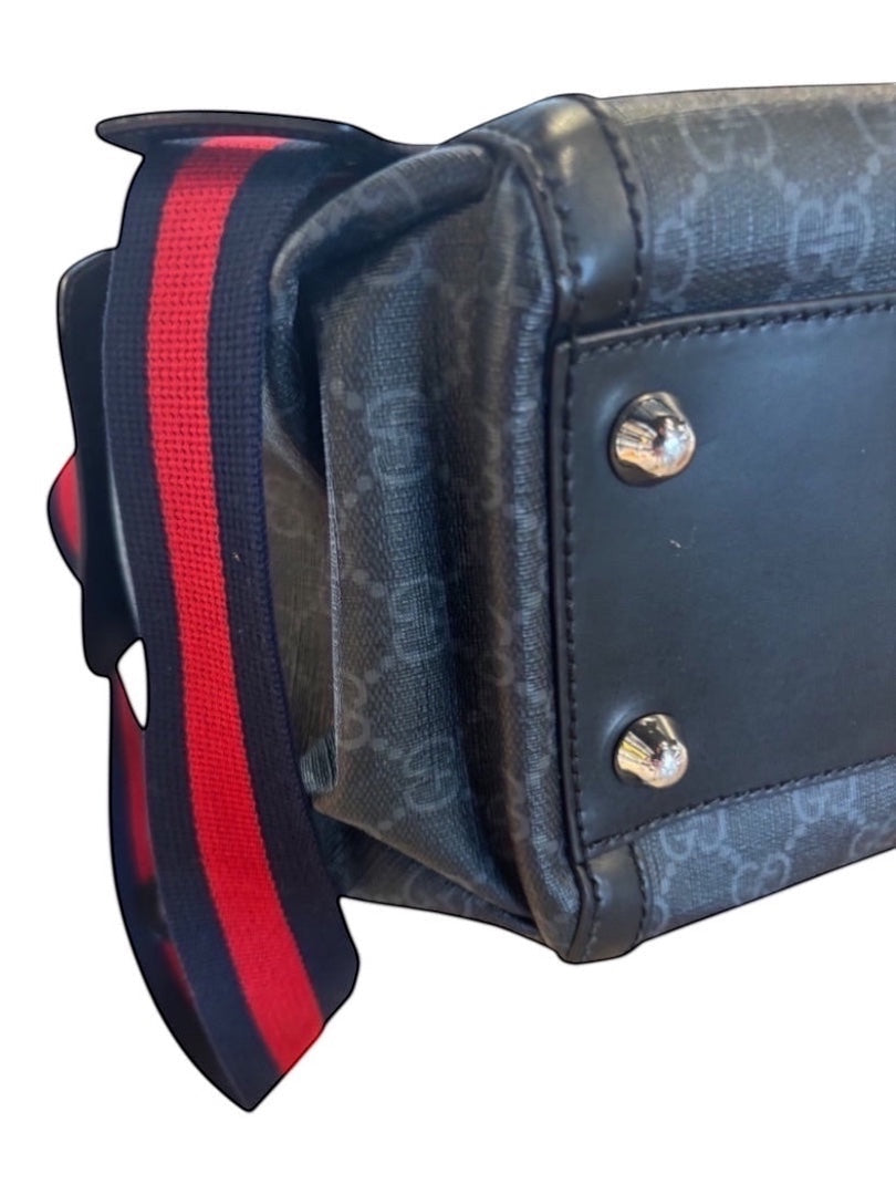 Posh Purse Co black canvas messenger bag with signature pattern, leather trim, and red/blue striped adjustable strap.