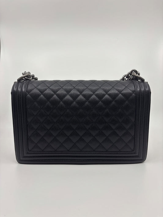 Posh Purse Co. large black Chanel Boy Bag in caviar leather with quilted diamond pattern and chain strap.