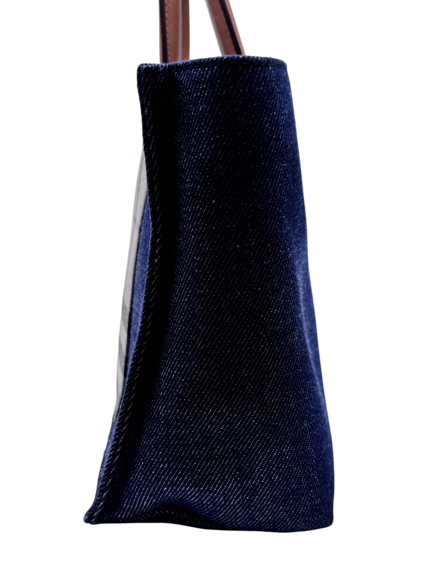 Side view of a Posh Purse Co Burberry Nova Check denim tote bag featuring dark blue denim and brown leather handles.