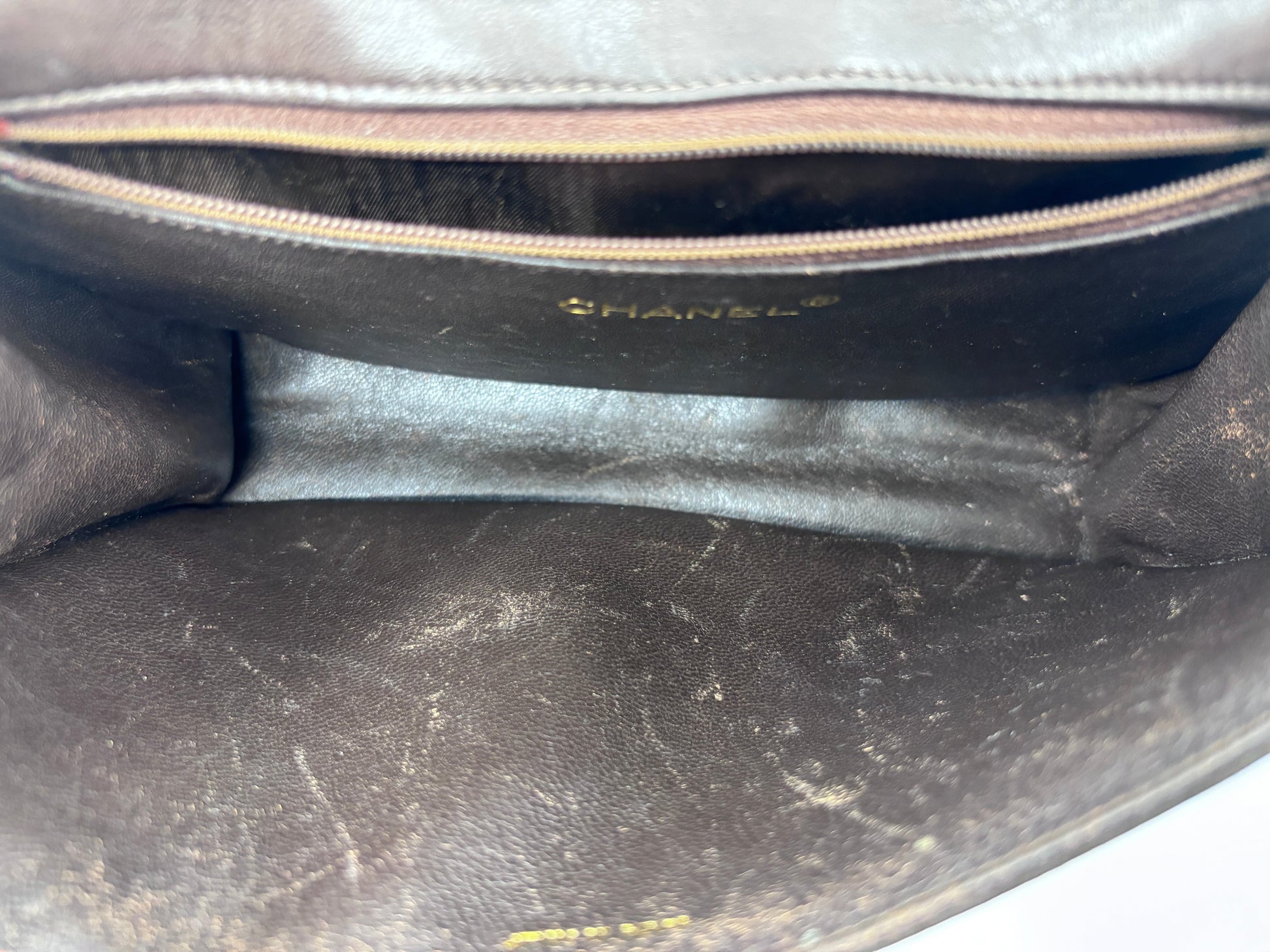 Interior of a preloved brown Chanel Timeless Flap bag from Posh Purse Co showing signs of wear, marks, and scratches.