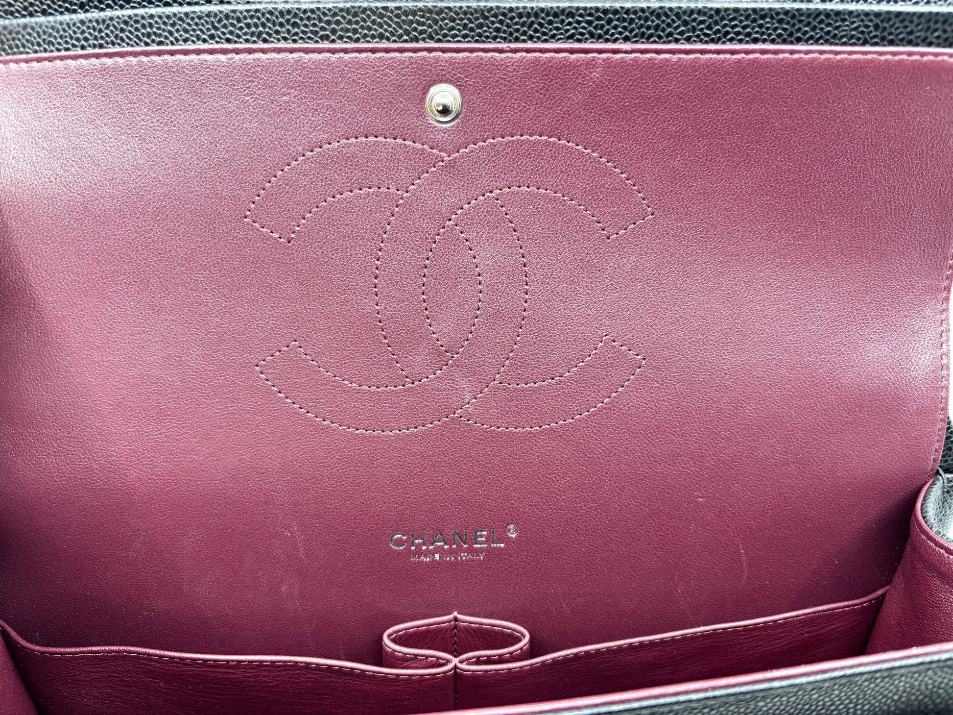 Interior of Posh Purse Co black Chanel Jumbo Flap bag featuring burgundy lining with embossed CC logo and stamp