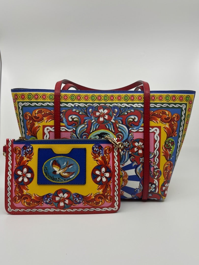 Dolce & Gabbana Dauphine Escape tote bag with red straps and a matching yellow pouch featuring a bird motif. Colorful floral and baroque print.