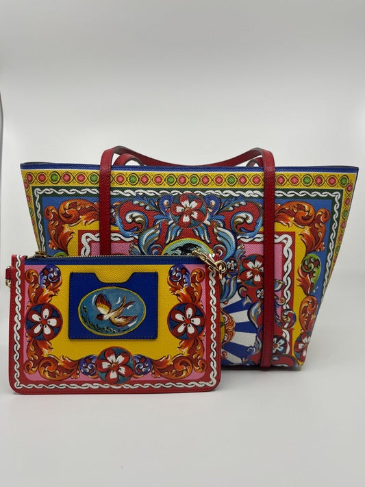Dolce & Gabbana Dauphine Escape tote bag with red straps and a matching yellow pouch featuring a bird motif. Colorful floral and baroque print.