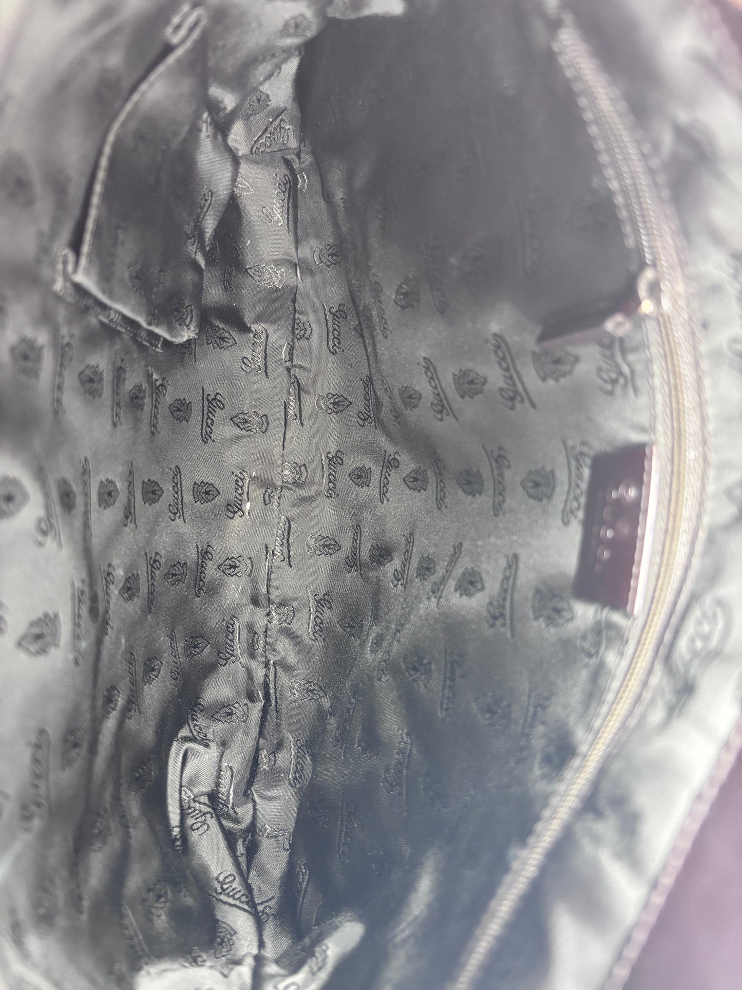 Interior lining of a Posh Purse Co Gucci shoulder bag featuring black fabric with a repeating Gucci logo pattern