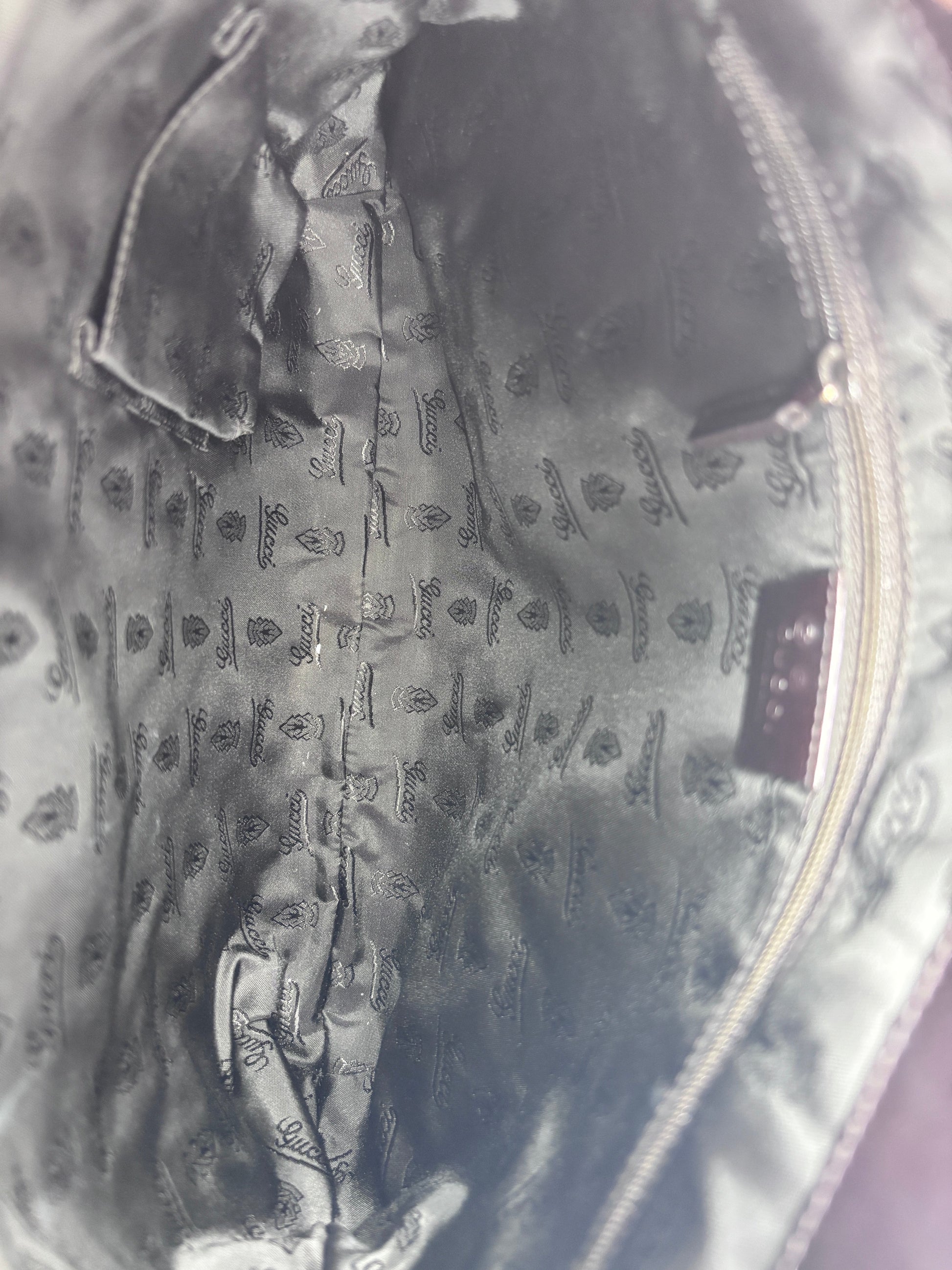 Interior lining of a Posh Purse Co Gucci shoulder bag featuring black fabric with a repeating Gucci logo pattern