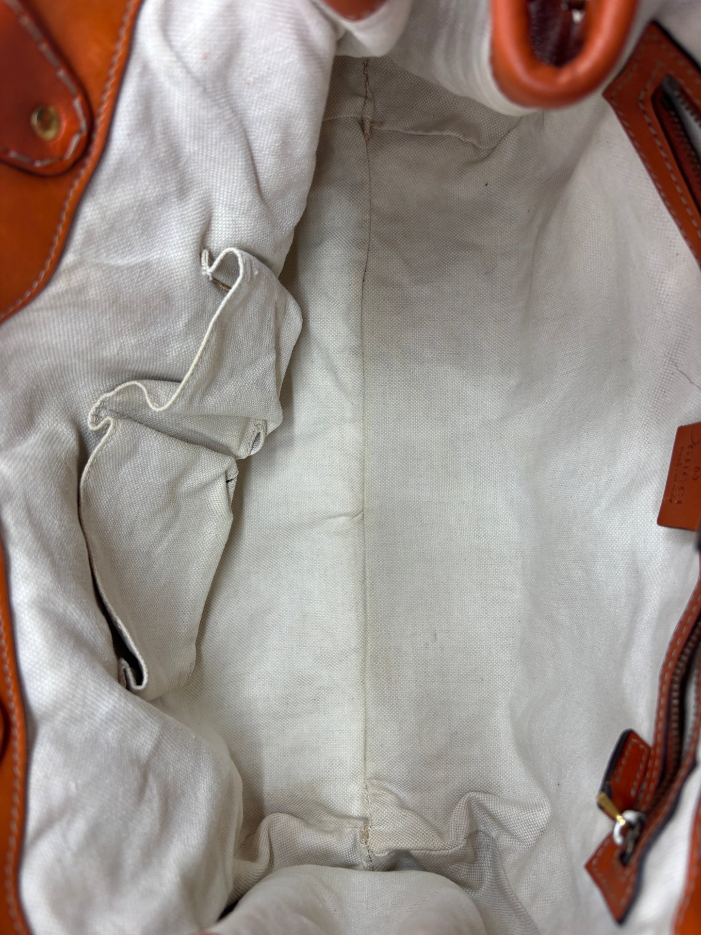 Interior view of a Posh Purse Co. preloved orange Gucci GG Running tote bag with a cream canvas lining and pockets.