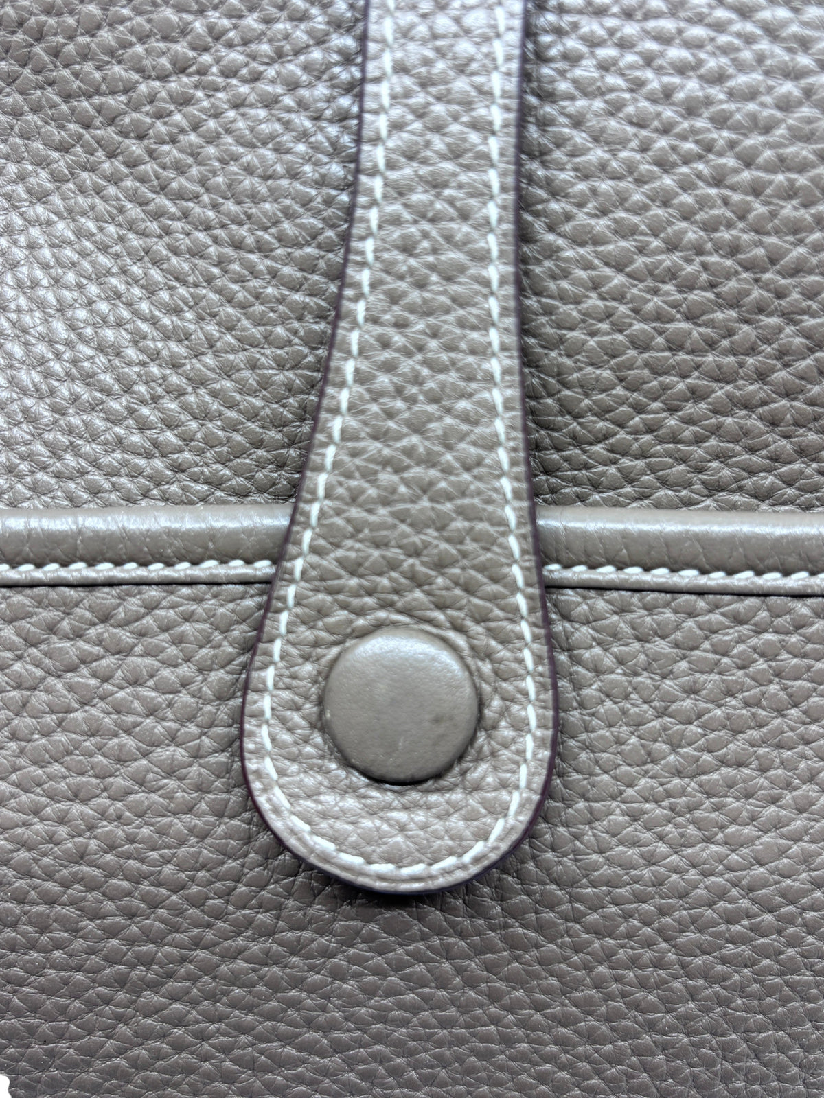 Close-up of the Etoupe Taurillon Clemence leather and snap button closure on a Posh Purse Co. Hermès Evelyne PM bag.
