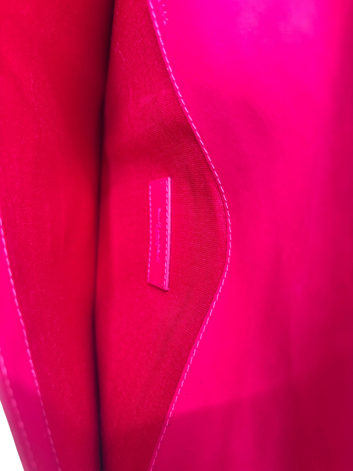 Interior of a vibrant pink Posh Purse Co Saint Laurent Bellechasse clutch with a matching leather brand logo tag.