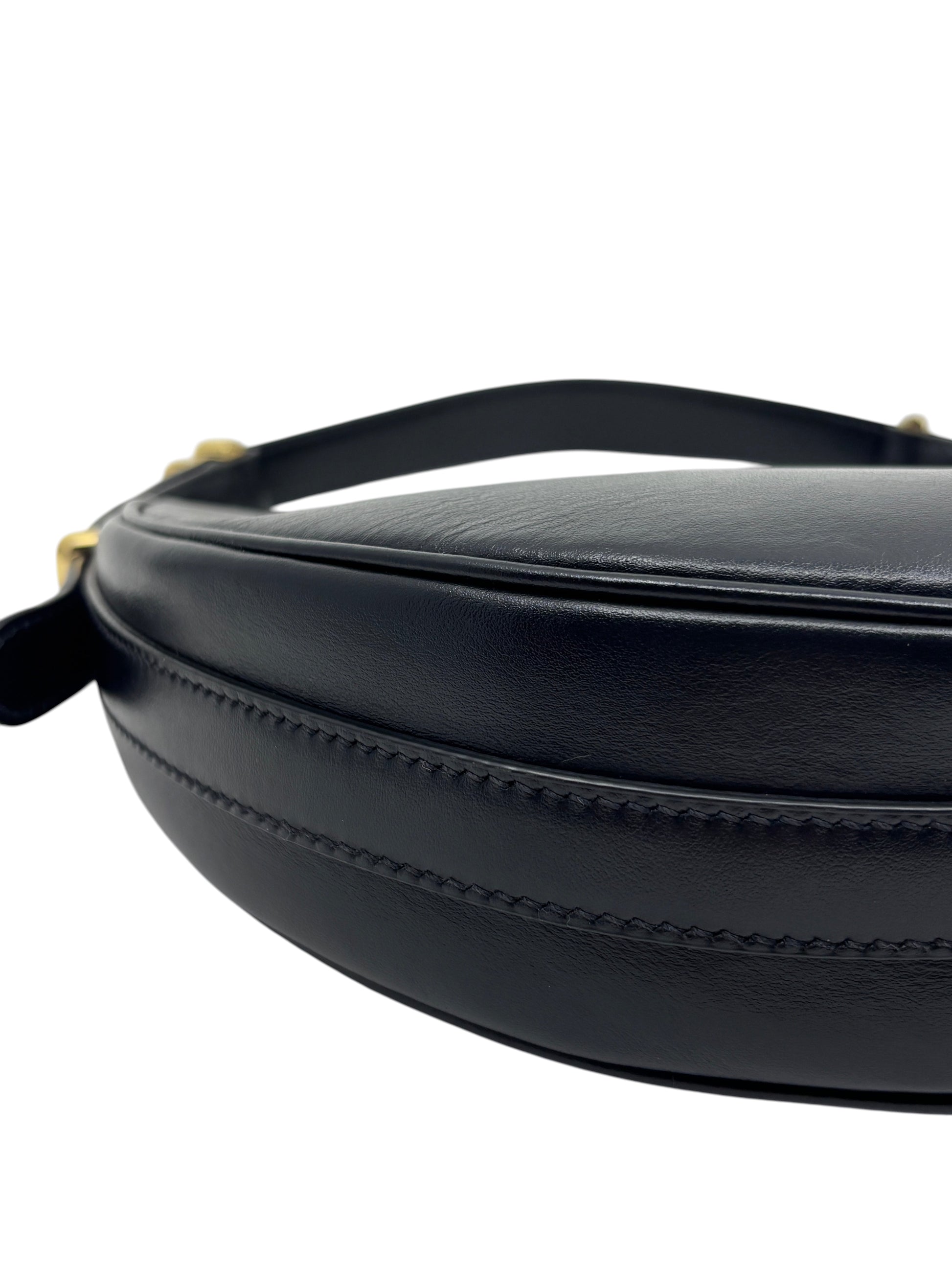 Close-up of the curved black leather silhouette of a Posh Purse Co. Prada Arqué shoulder bag with gold hardware.
