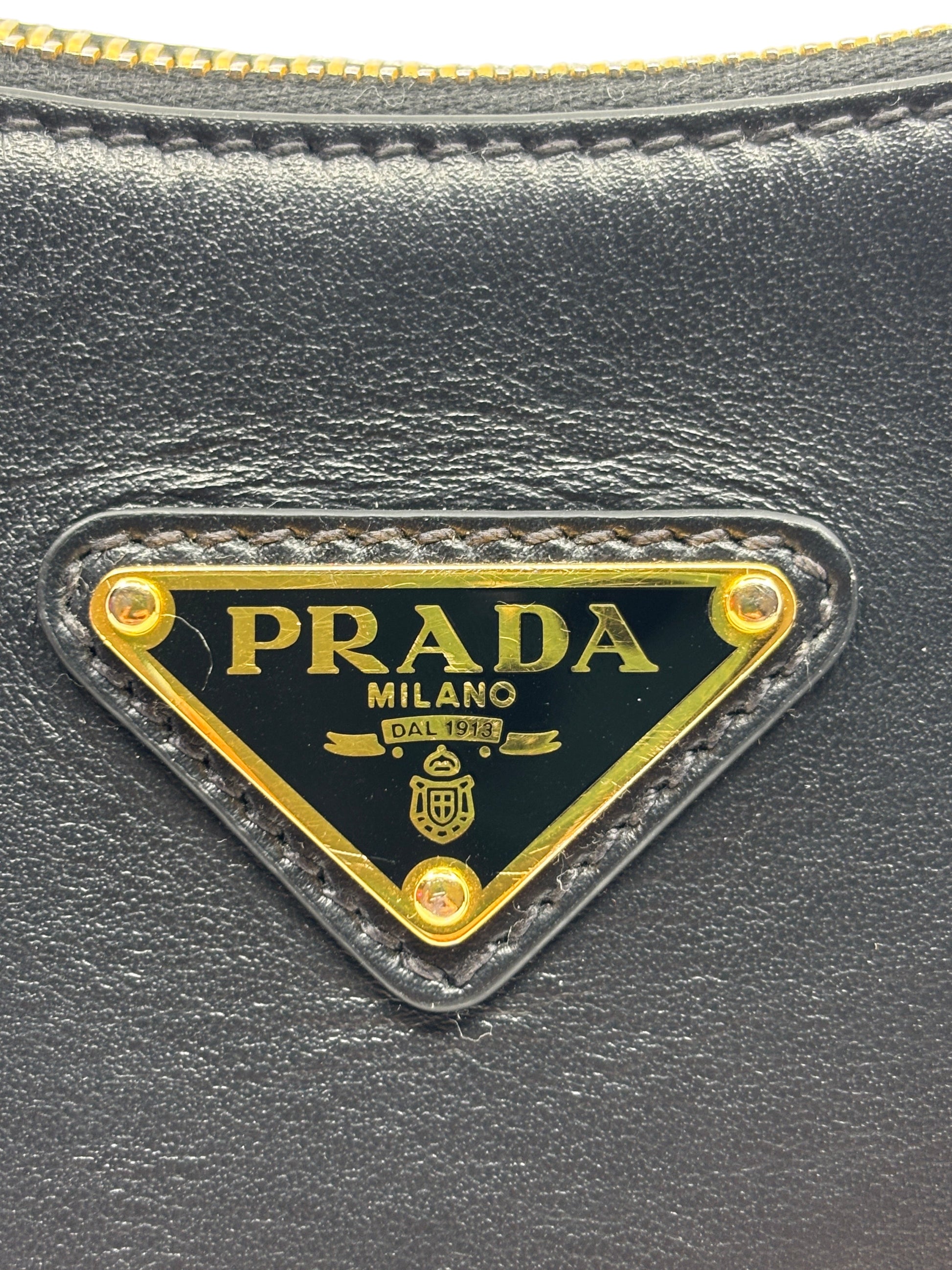 Posh Purse Co. Prada Arqué bag featuring the iconic gold-tone triangular logo plaque on smooth black leather.
